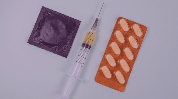 Seringa, preservativo e remédios em cima de uma mesa verde.